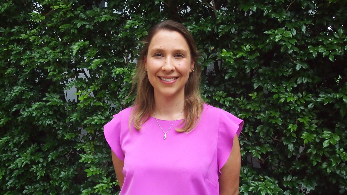 A smiling woman in a pink top in front of a hedge