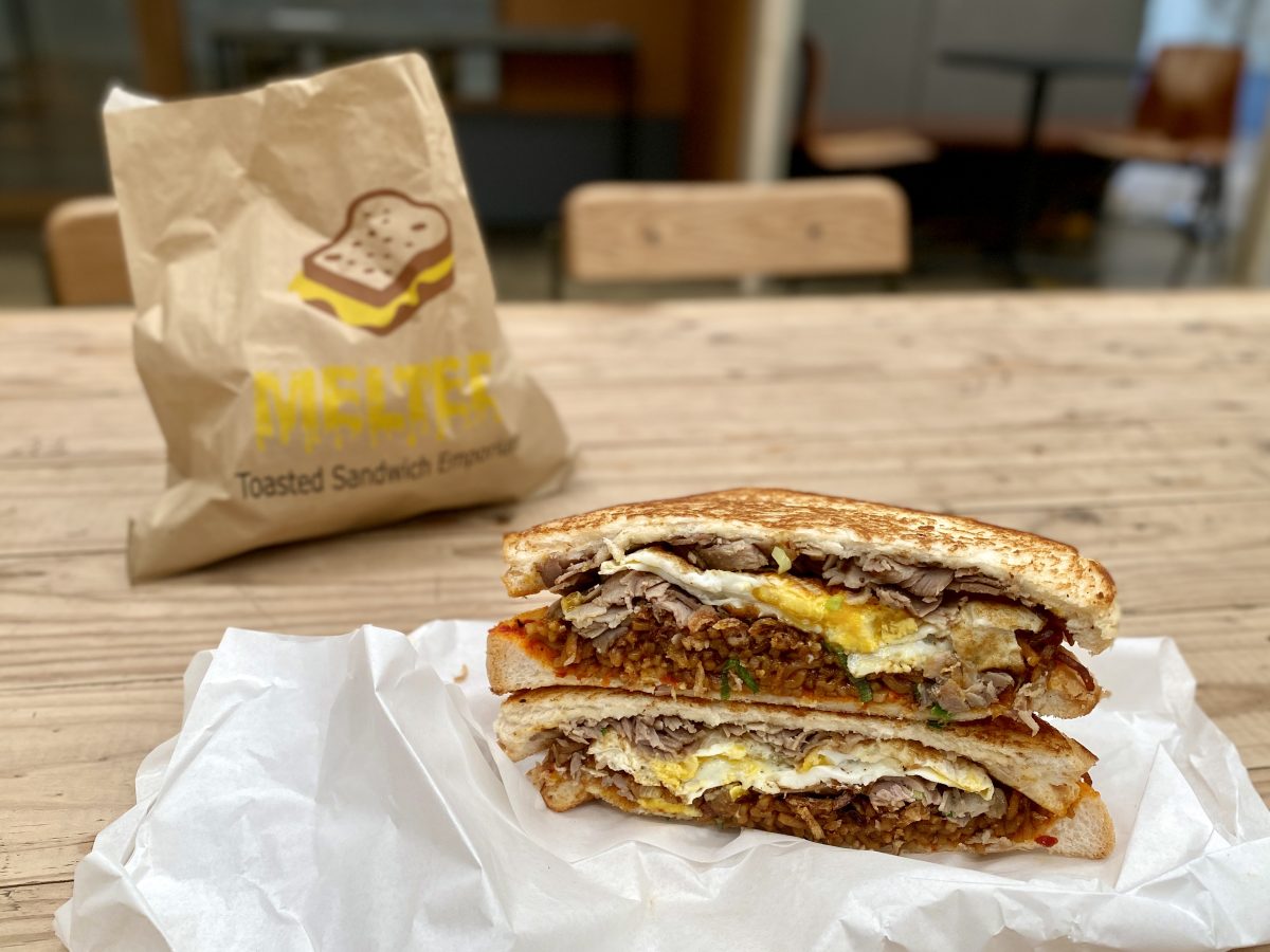 A toasted sandwich with egg, pork and noodles on a white paper bag. A Melted branded paper bag is in the background.