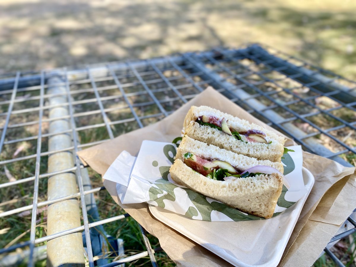 A tasty looking sandwich with figs with a paper bag on a wire rack table.