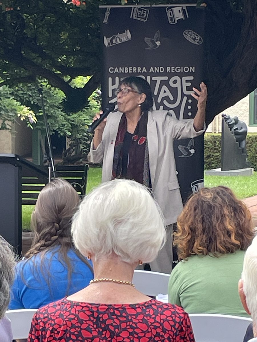 Woman speaking with microphone gesticulates in front of crowd