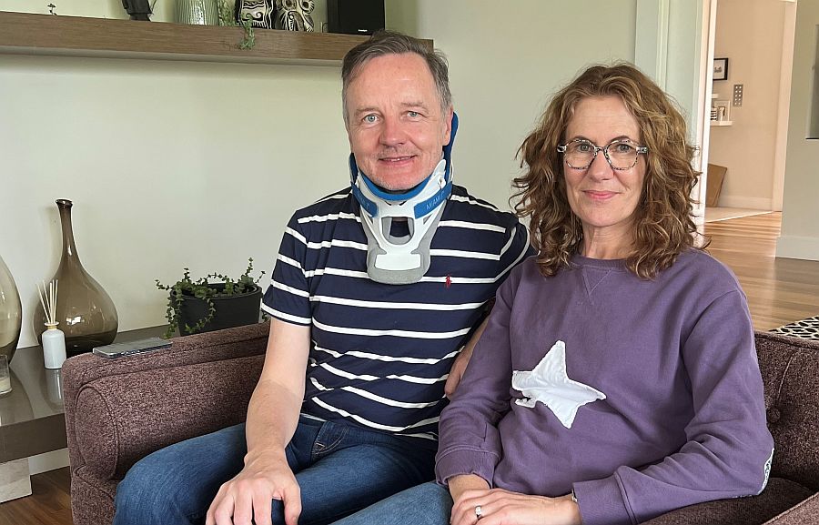 man with a neck brace sitting net to a woman on a lounge