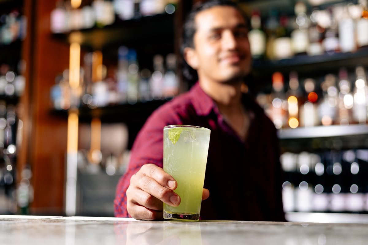 Man places cocktail on bar.