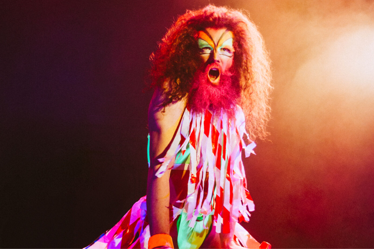 A long haired man with a beard wearing streamers and makeup