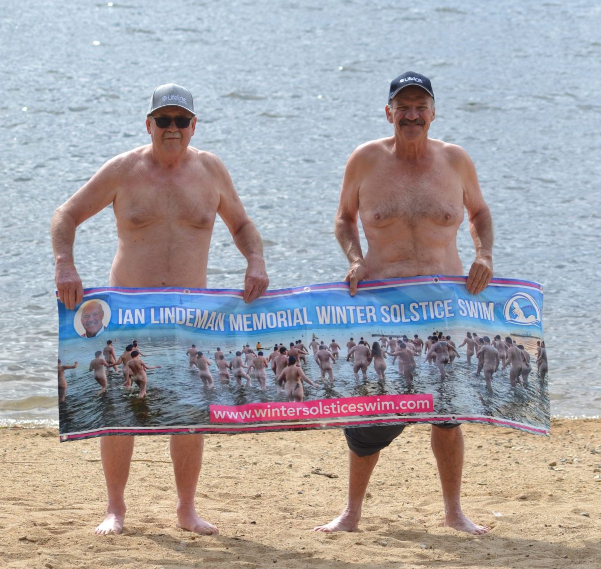 Men standing behind a poster for the Winter Solstice Swim