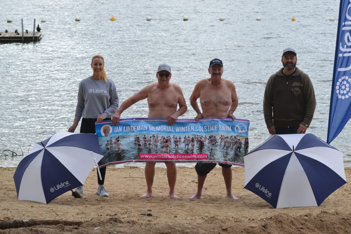 Men standing behind a poster for the Winter Solstice Swim