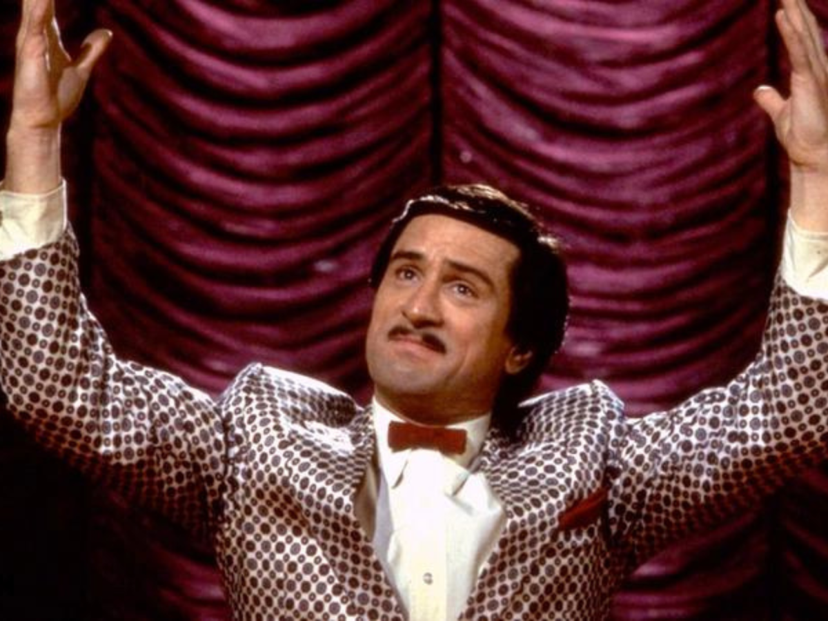 Still from The King of Comedy showing a man on a stage raising his hands