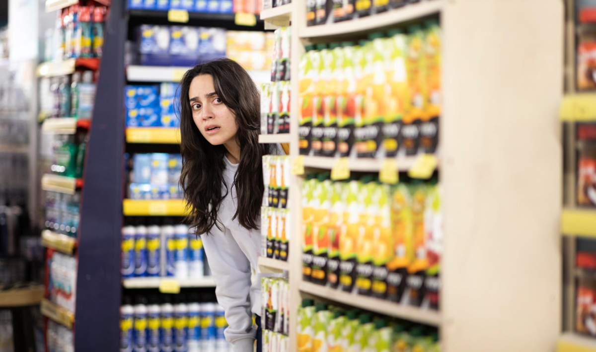 Still from The Persian Version showing a woman leaning out from a supermarket aisle