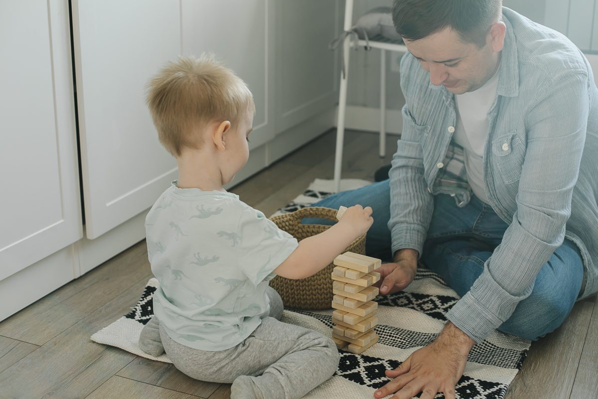 Happy father and toddler boy child little son playing with wooden blocks in children room at home