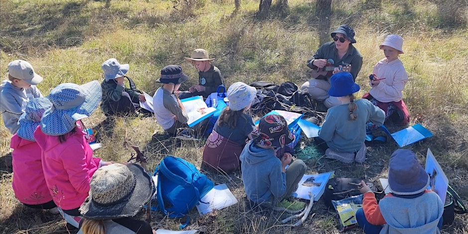 Group of kids sitting in a circle while a Ginninderry Conservation Trust ranger sings them a song.