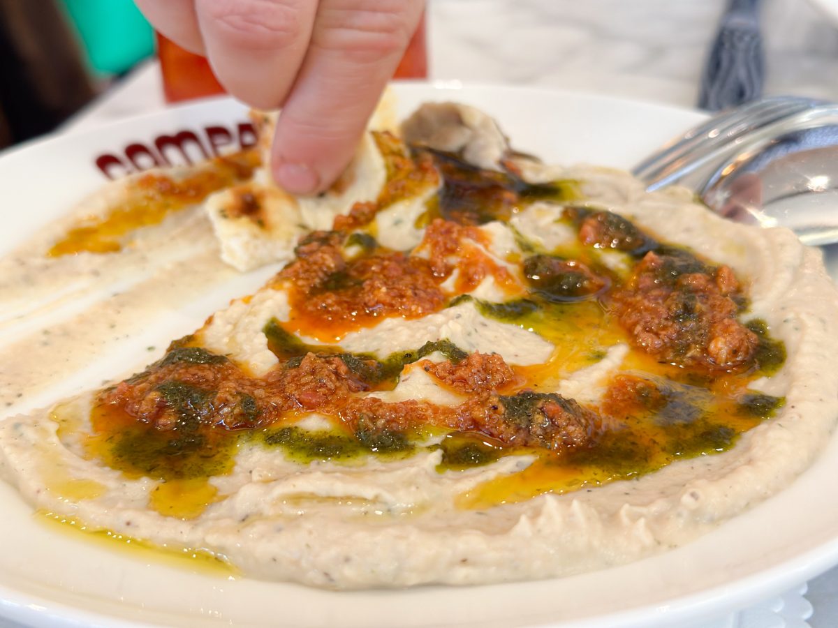 A hand swipes bread through a dip on a plate.