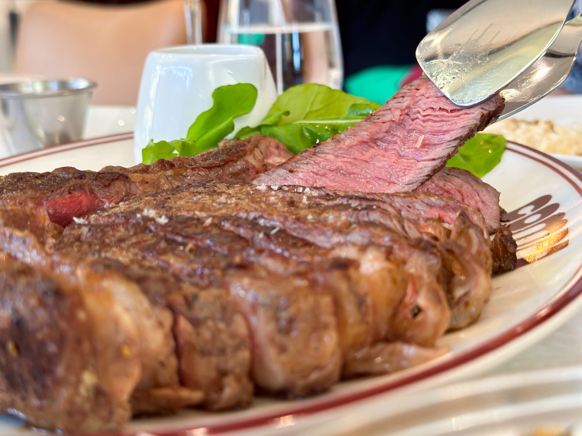 slice of rare beef being taken from a plate of steak with tongs.