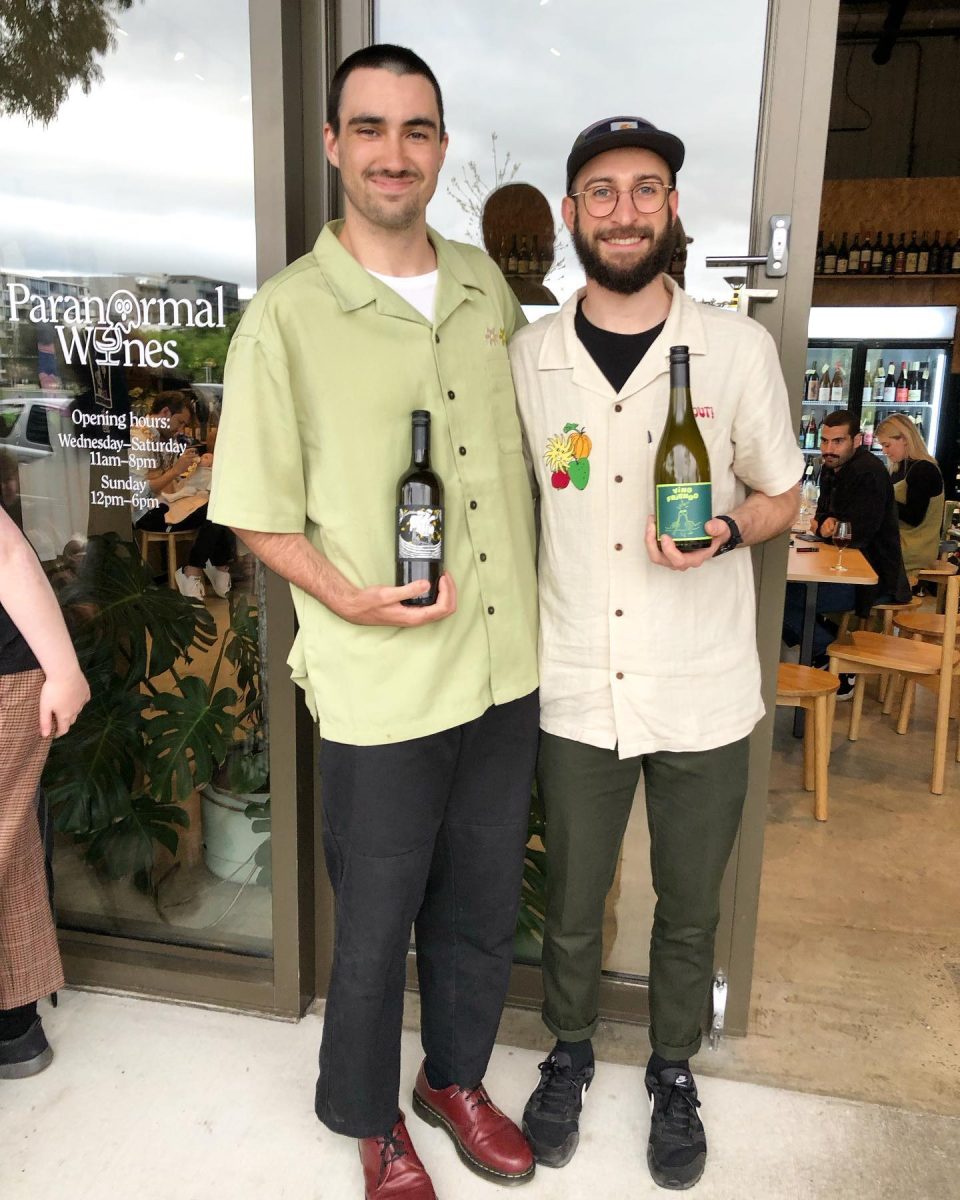 Two men hold bottles of wine outside a bar