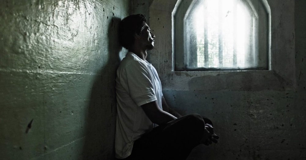 Still from A Boy Called Piano showing a man in a prison cell looking out a barred window