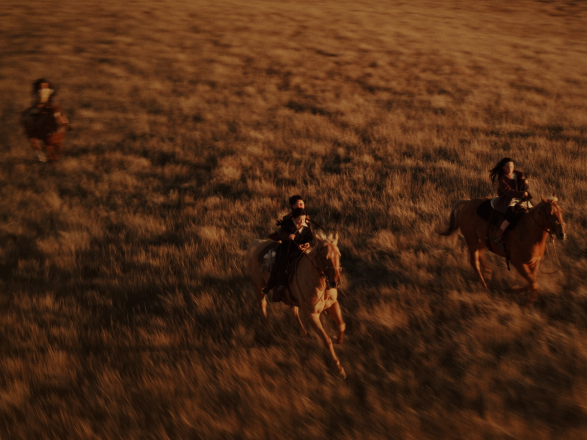 Aerial still from Bones of Crows showing a small group on horseback on a plain