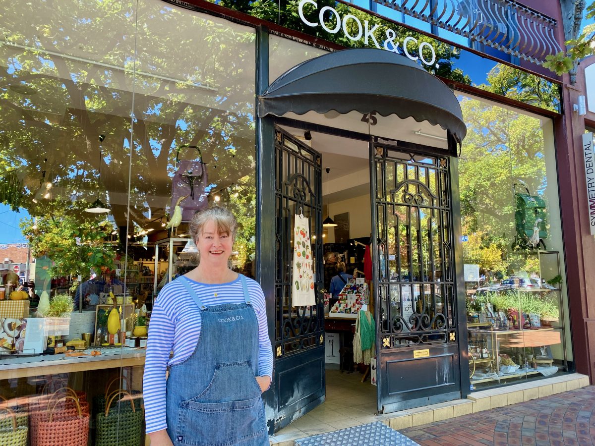Claire wears a branded apron and stands in front of the Cook & Co shop