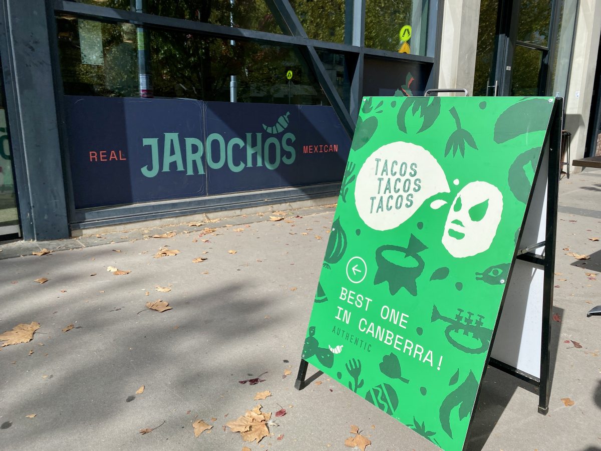 A-fram sign covered with green cartoon images with the Jarochos restaurant in the background. 