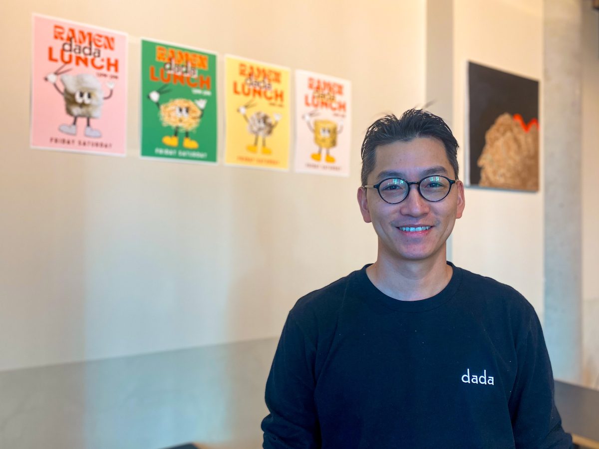 Man with glasses stands in front of colourful posters with ramen