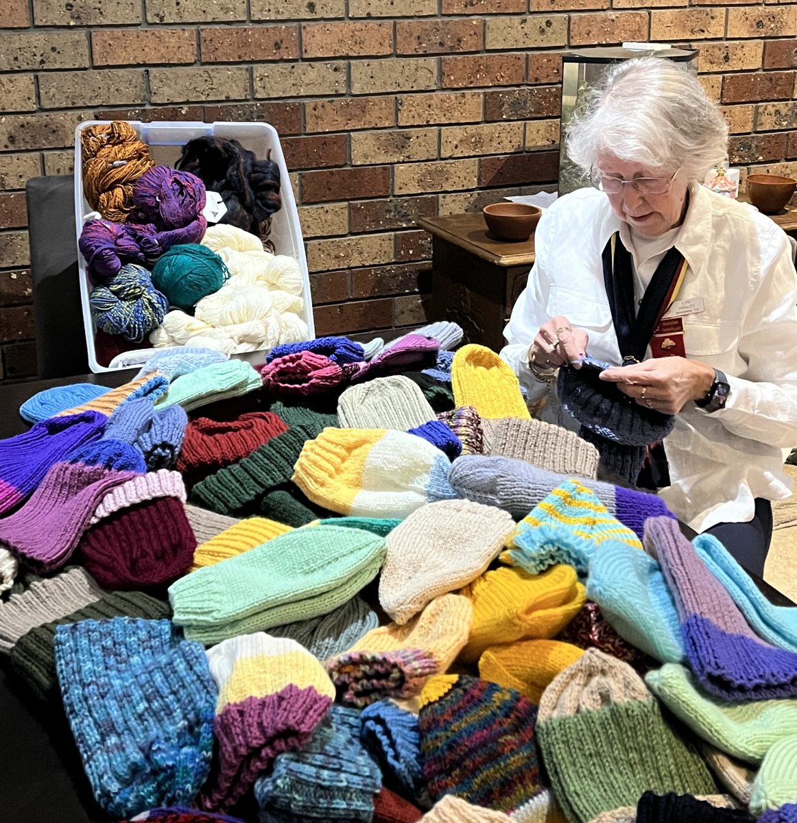 Lyn Hanley knitting surrounded by beanies