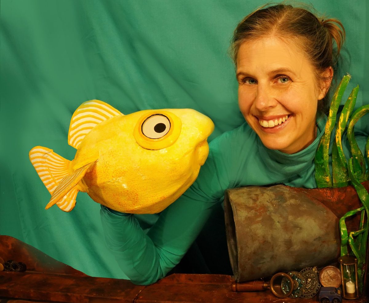 Woman holding yellow fish puppet on green backdrop