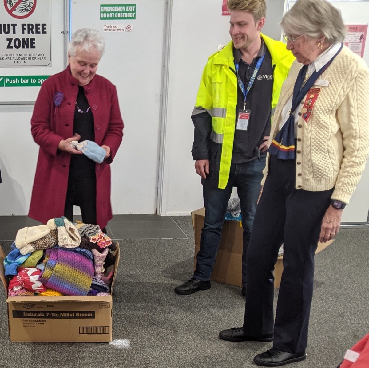 Two women and a man in high-vis looking at a box of beanies