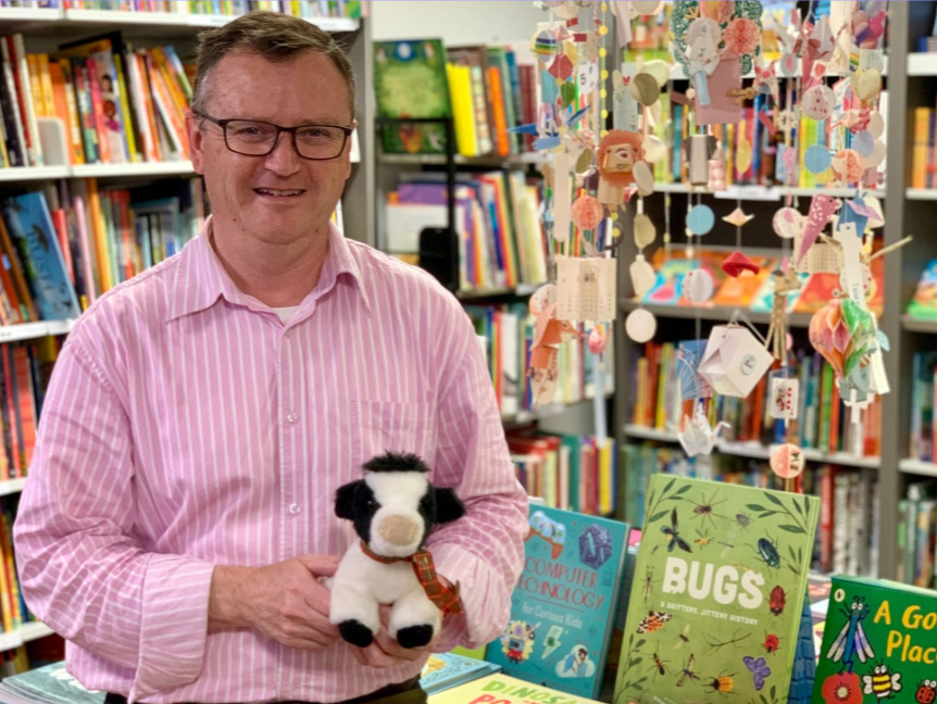 Man standing in book store holding a toy cow.