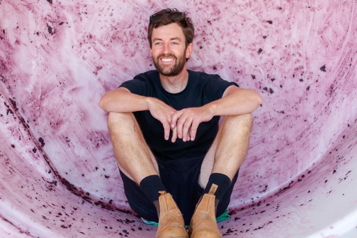 Nathan sits in a round barrel stained with red grapes.