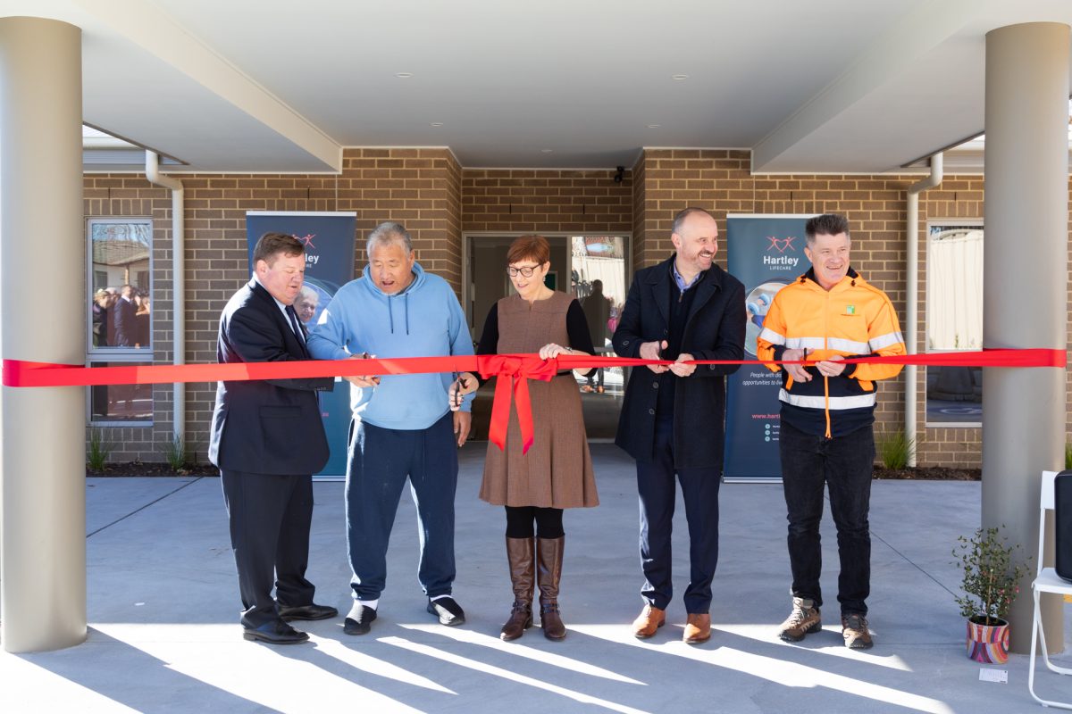 Five people cutting ribbon at house opening event