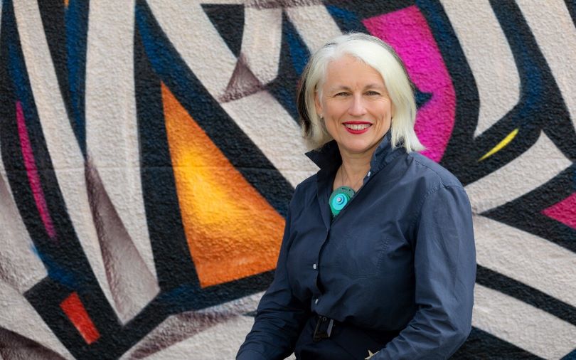 A woman with grey hair in front of a colourful background.