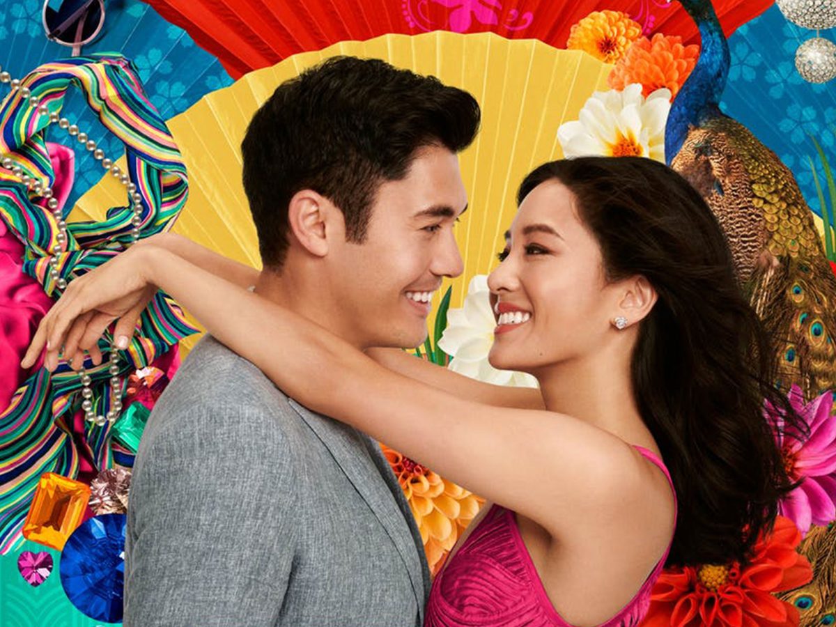 Promotional still from Crazy Rich Asians showing a couple embracing in front of a background of colourful fans