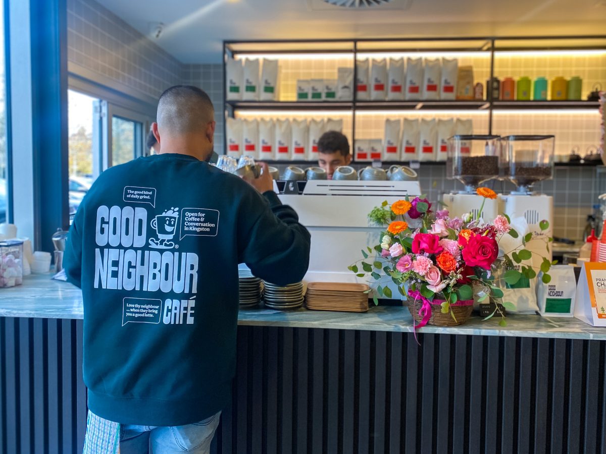 Man in Good Neighbour branded sweatshirt at coffee counter.