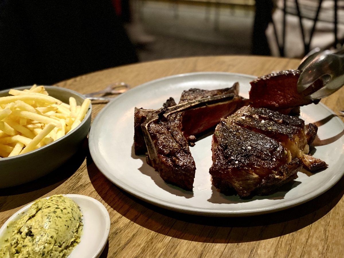 A good looking steak, sliced, with butter in a dish and a bowl of fries.