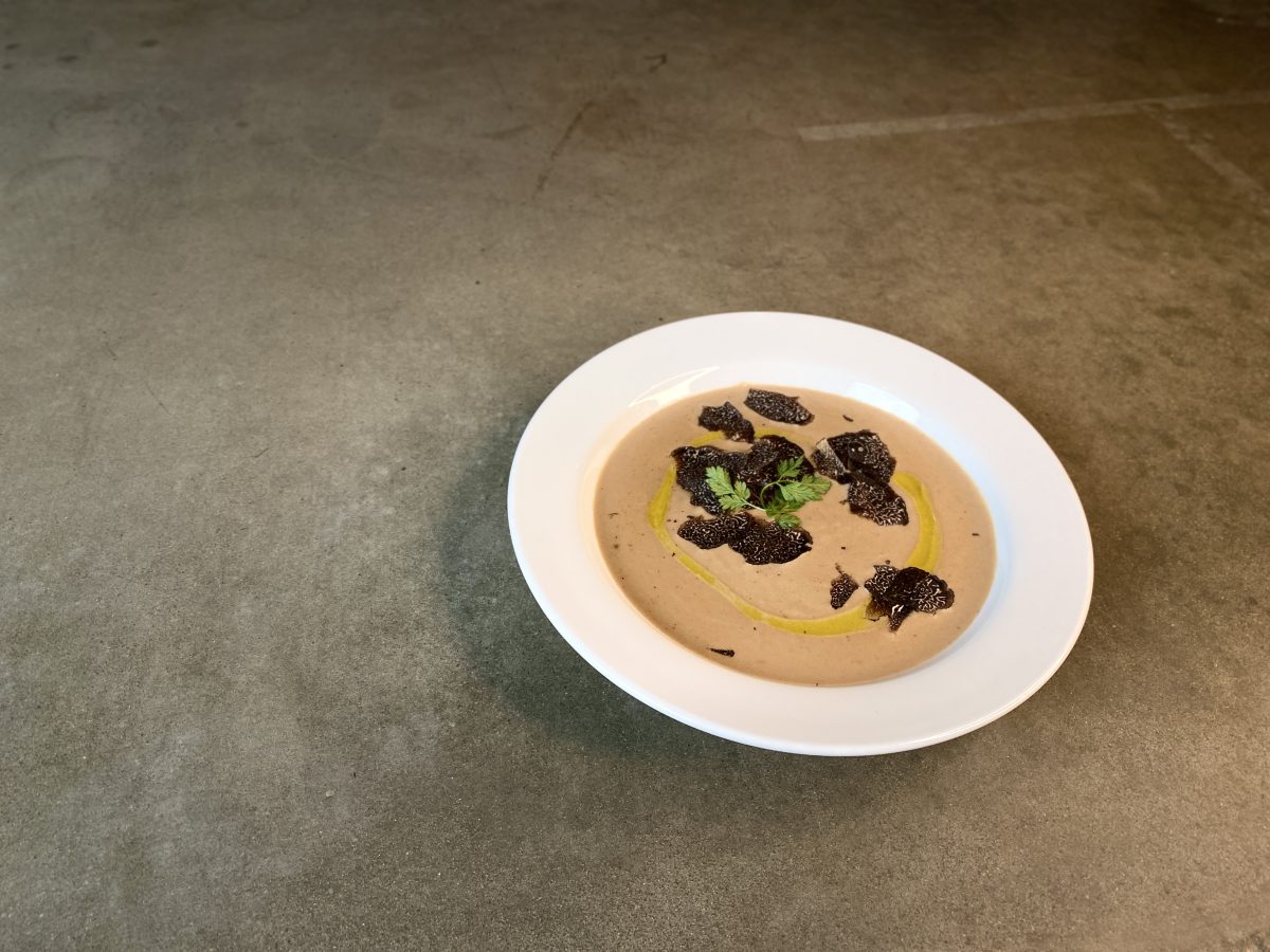 Bowl of soup with shaved truffles and herb garnish.