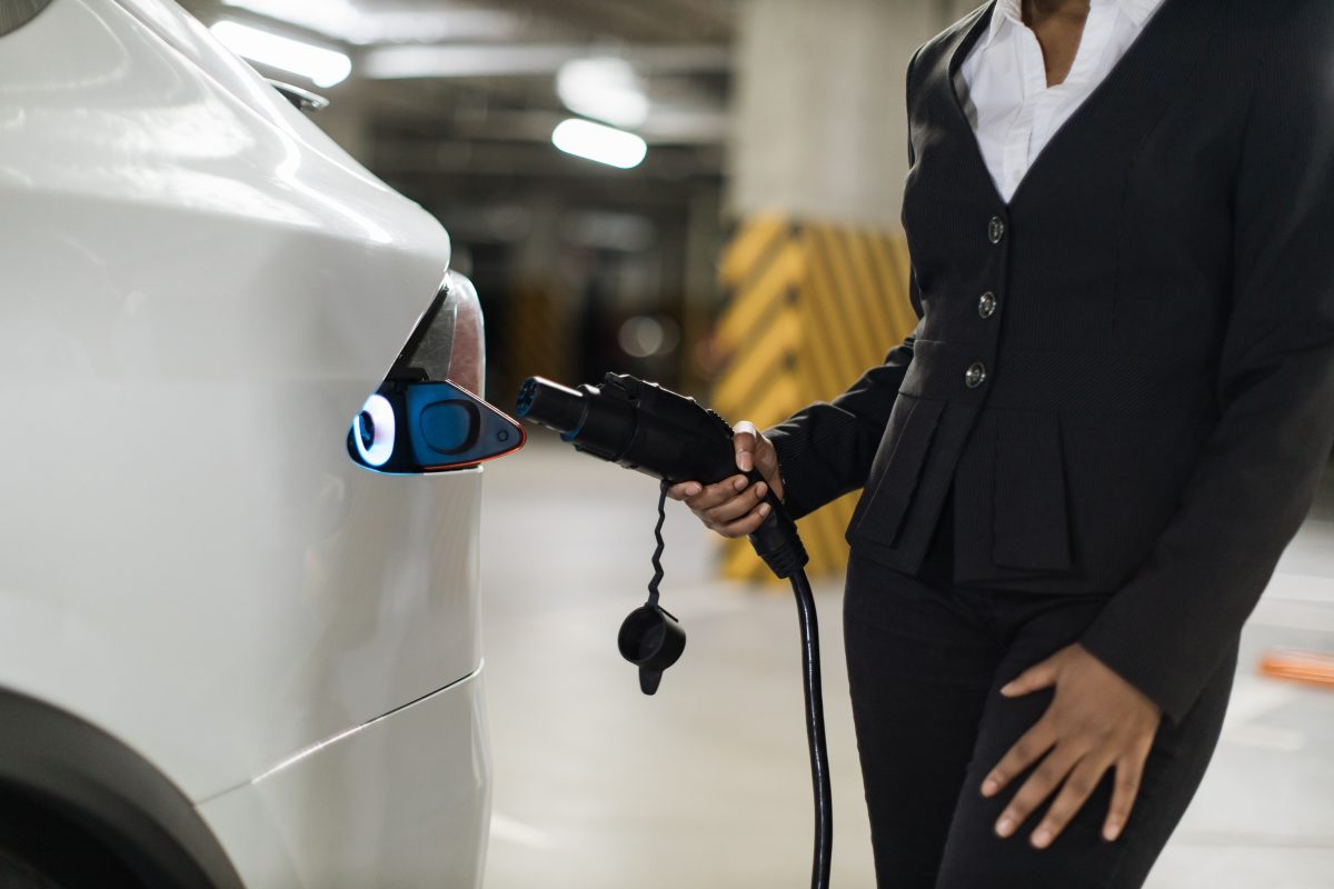Woman with connector cord standing near e-car in garage