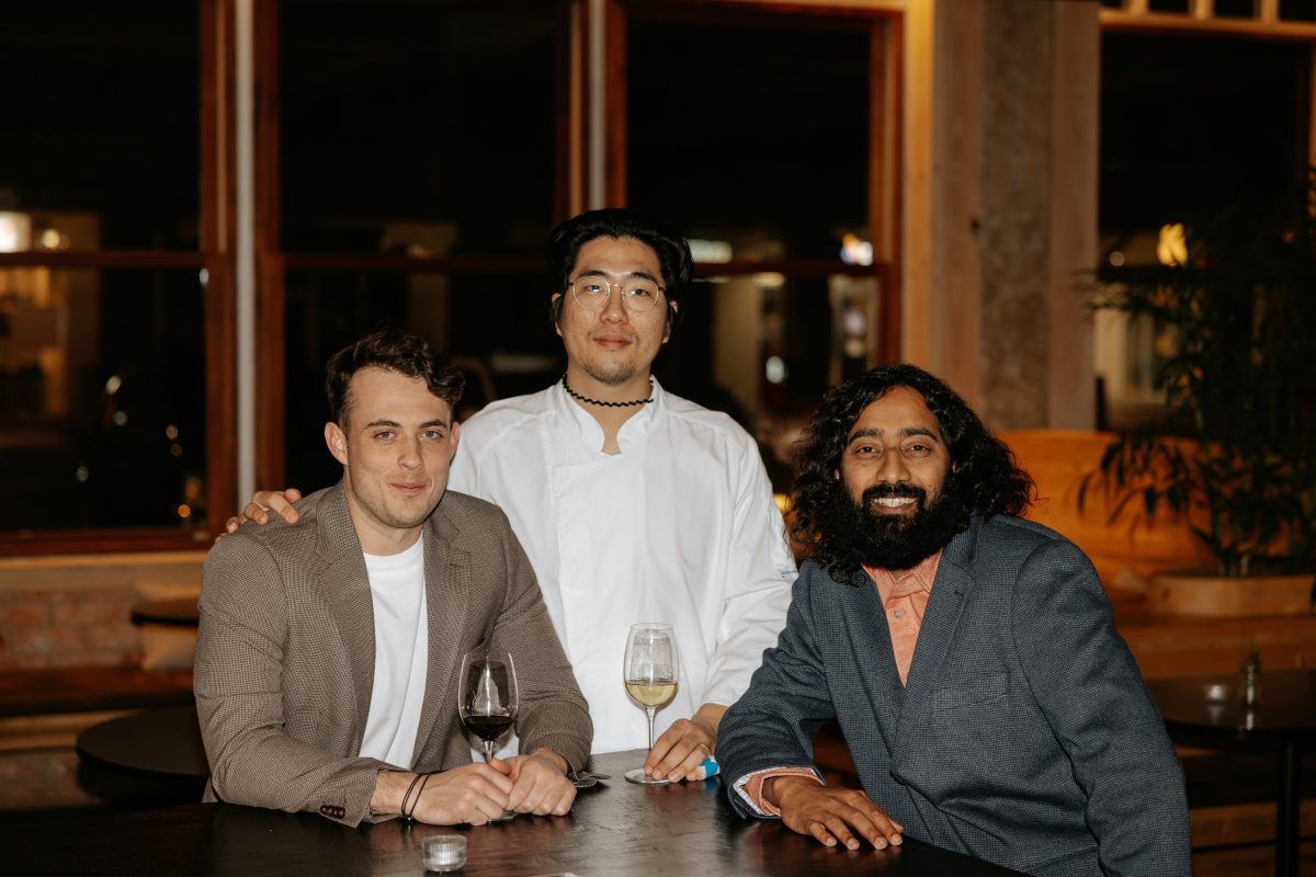 Three men pose in restaurant dining room.