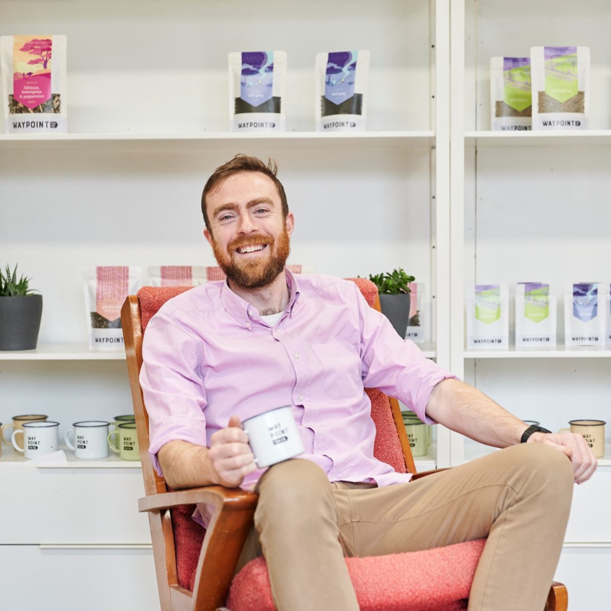 Finn sits in chair holding a Waypoint Tea branded tin mug