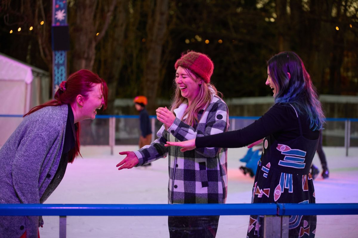 Three women laughing in an ice rink at night