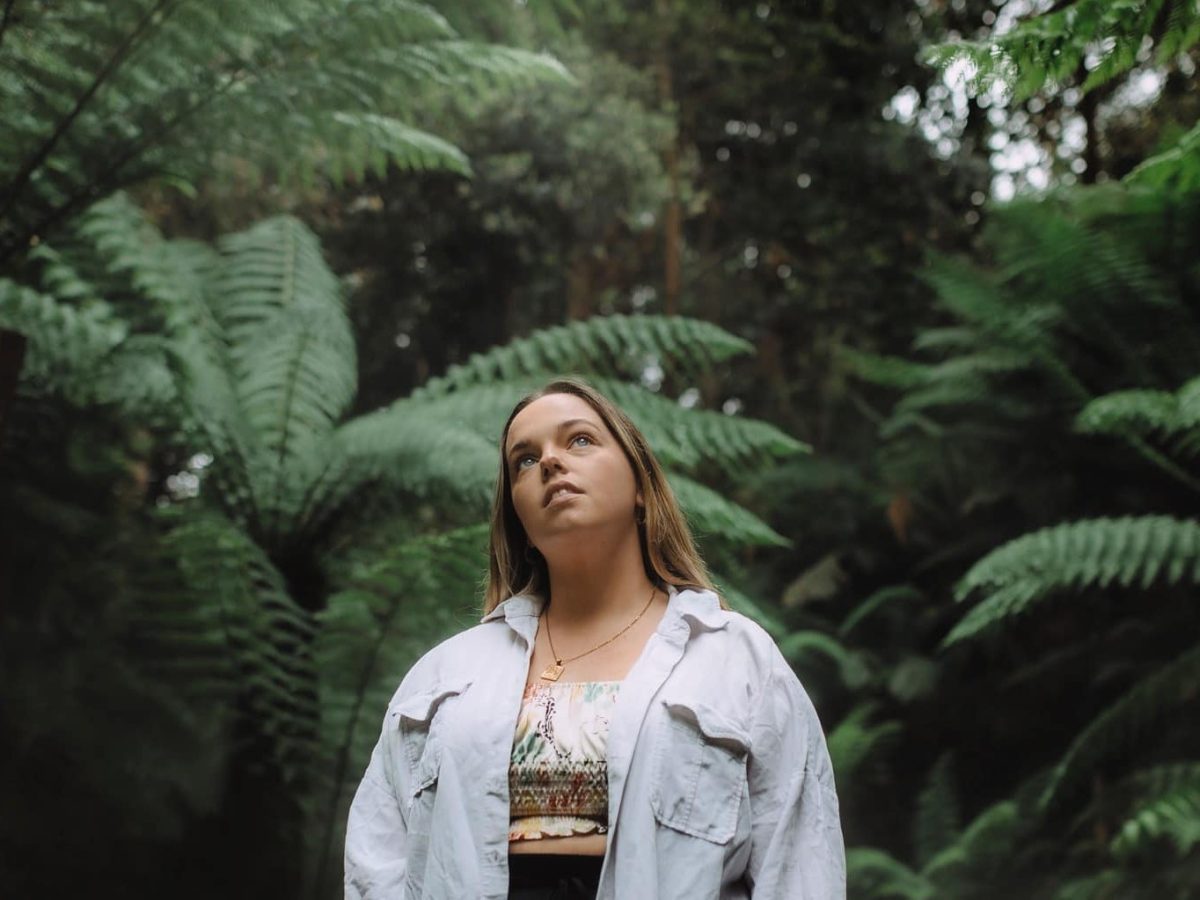 Sophie Edwards looks upward standing in front of a fern forest
