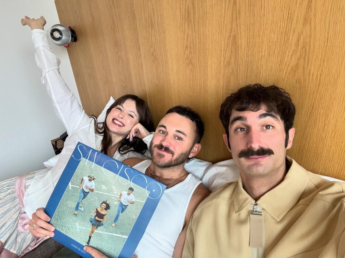 Three people hold a record and smile while taking a group selfie.
