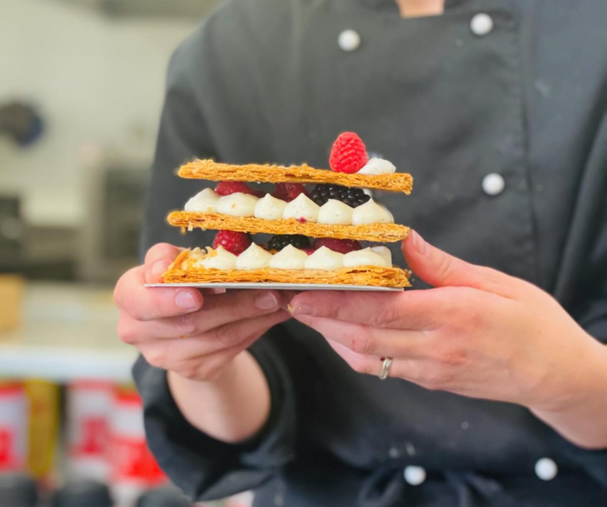 Hands holding a delicious looking pastry with layers of piped cream and berries.