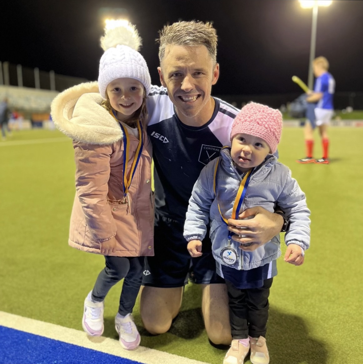 man on hockey field holding his two children