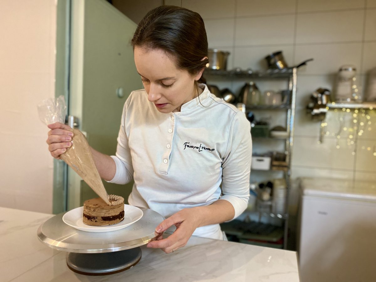 A woman in chef's jacket carefully piping chocolate mousse onto a cake. 