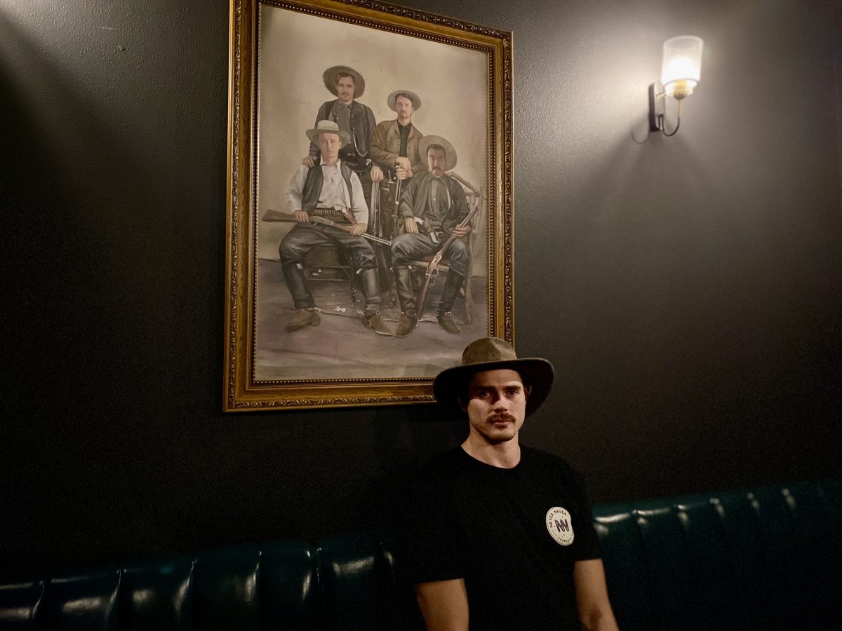 Man in hat sits in dark room in front of portrait