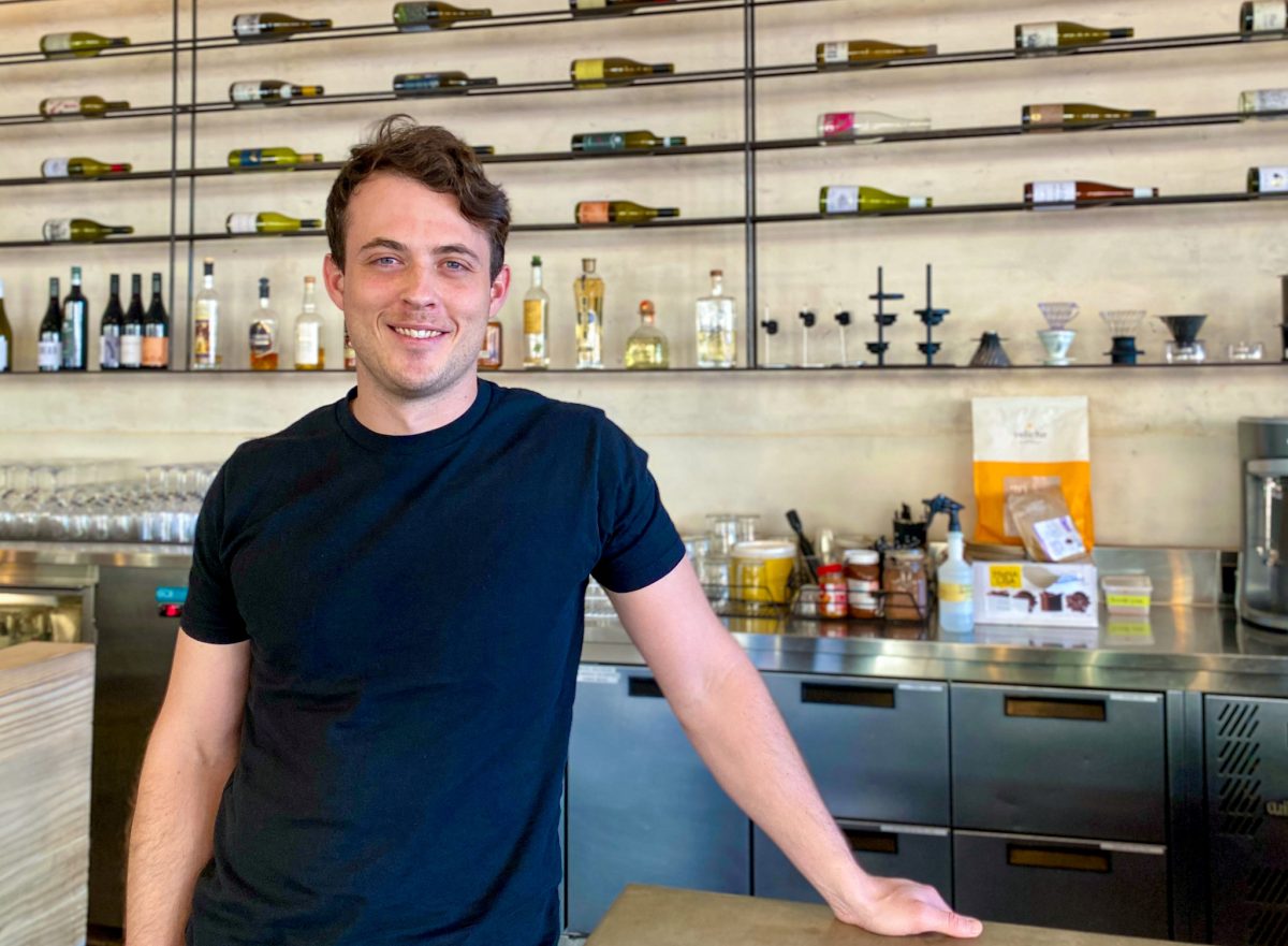 Lachlan smiles in front of wine bottles on wall.