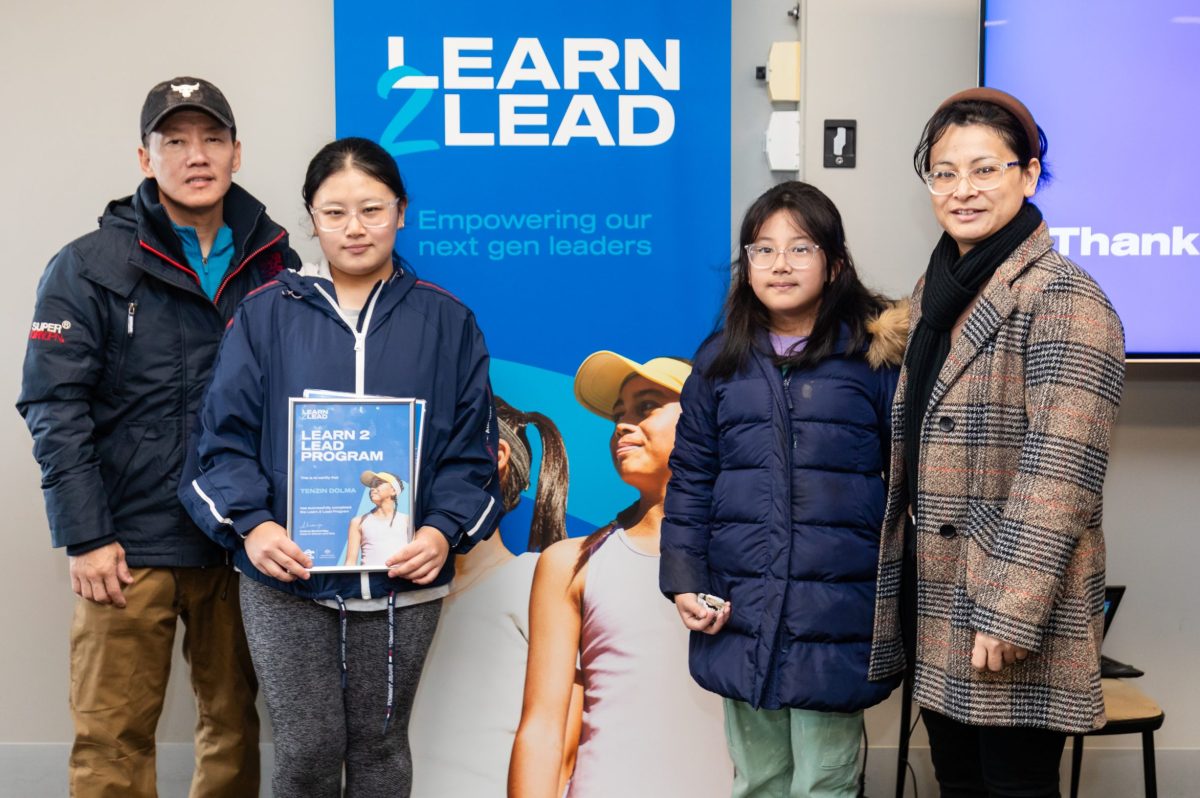 The Tenzin Dolma family from the Kippax Tennis Club in from of a Learn 2 Lead banner.