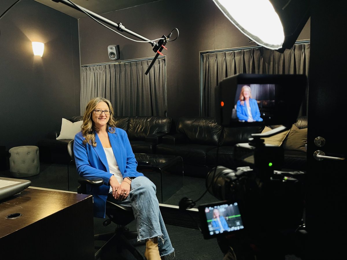 Fleur Ferris sits in a film studio amid TV screens, boom mic and lighting.