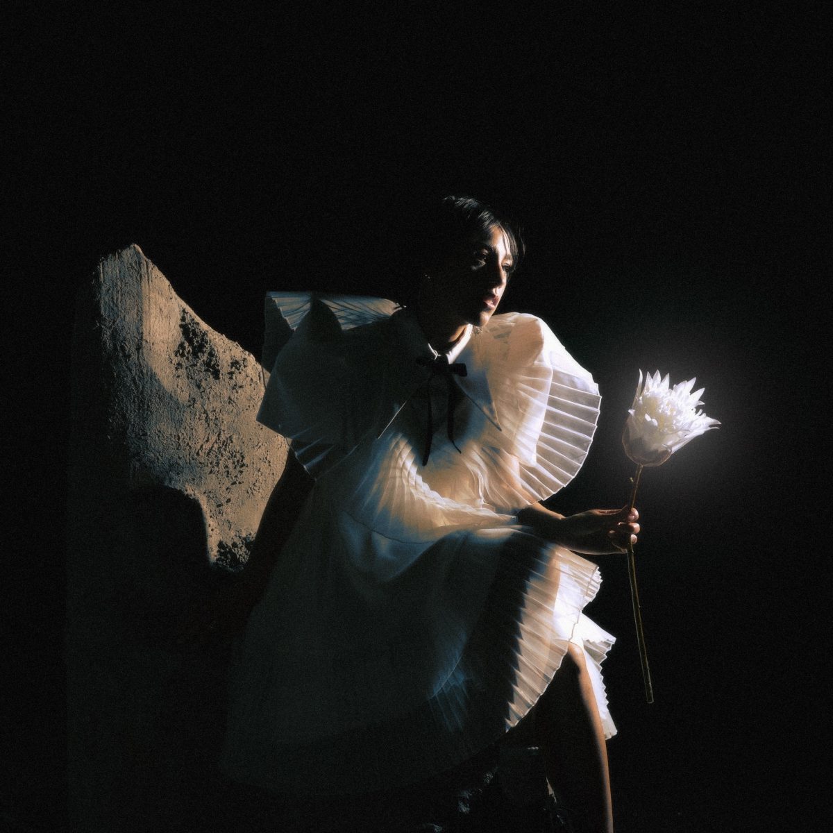 Telenova singer poses seated with white flowers in darkness