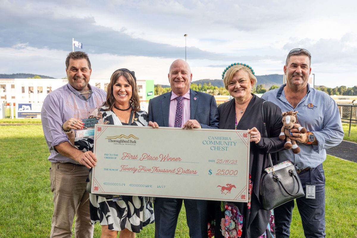 five people standing on a racecourse holding a large novelty cheque