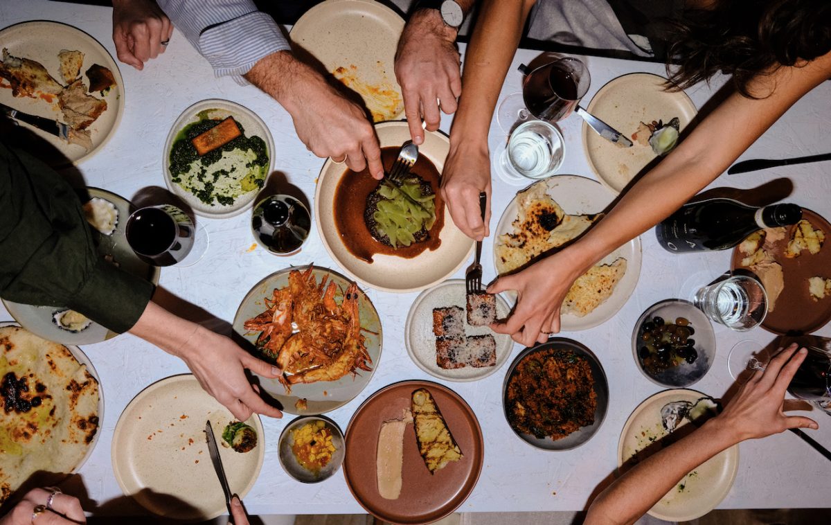 Photo from above of a chaotic table with many hands grabbing at different dishes.