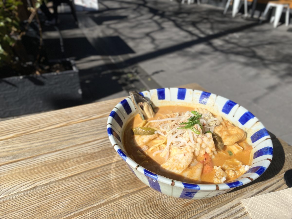 Bowl of laksa in blue and white striped bowl in the sunshine.