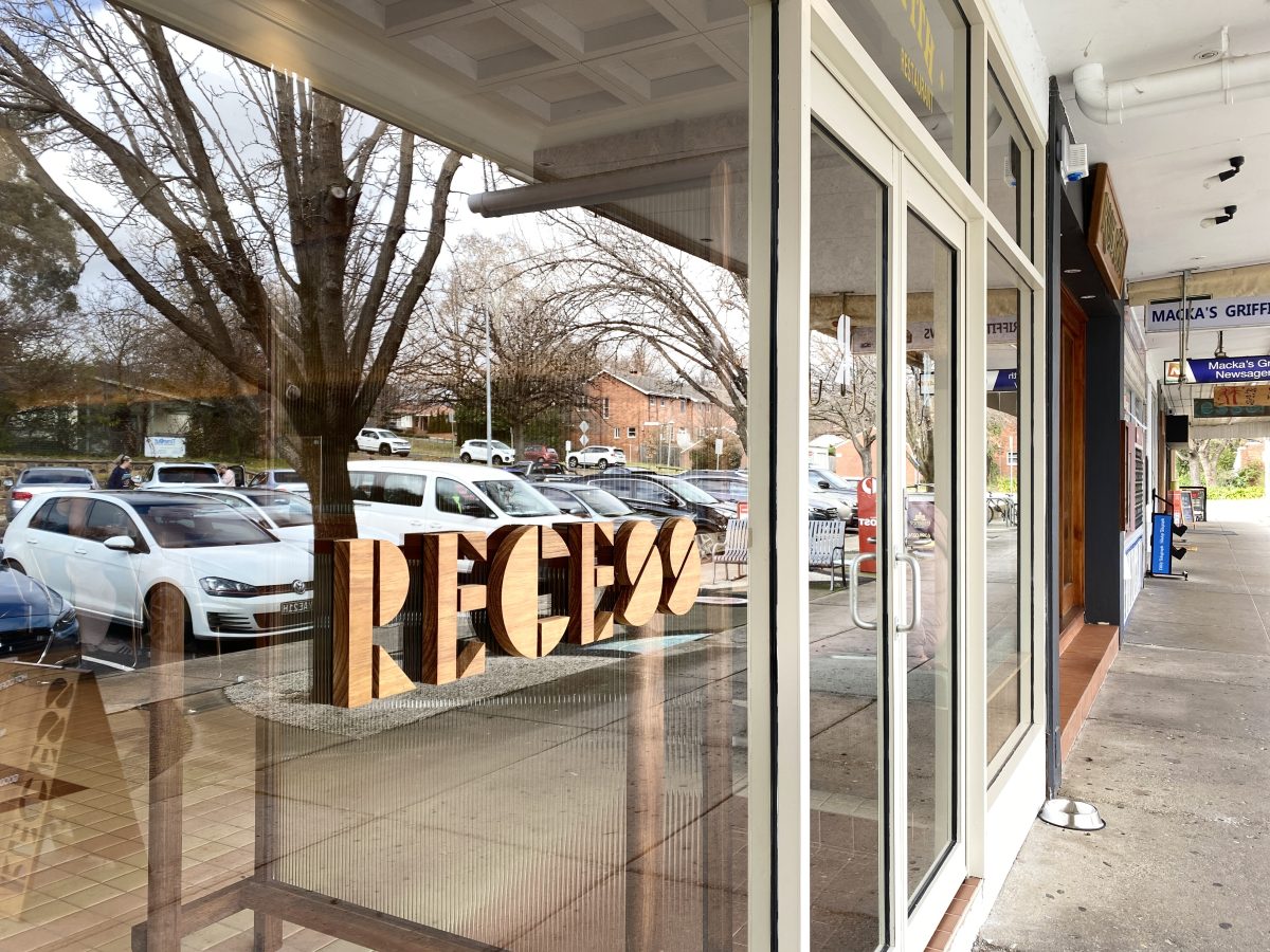 Wooden lettering spells RECESS on glass window.